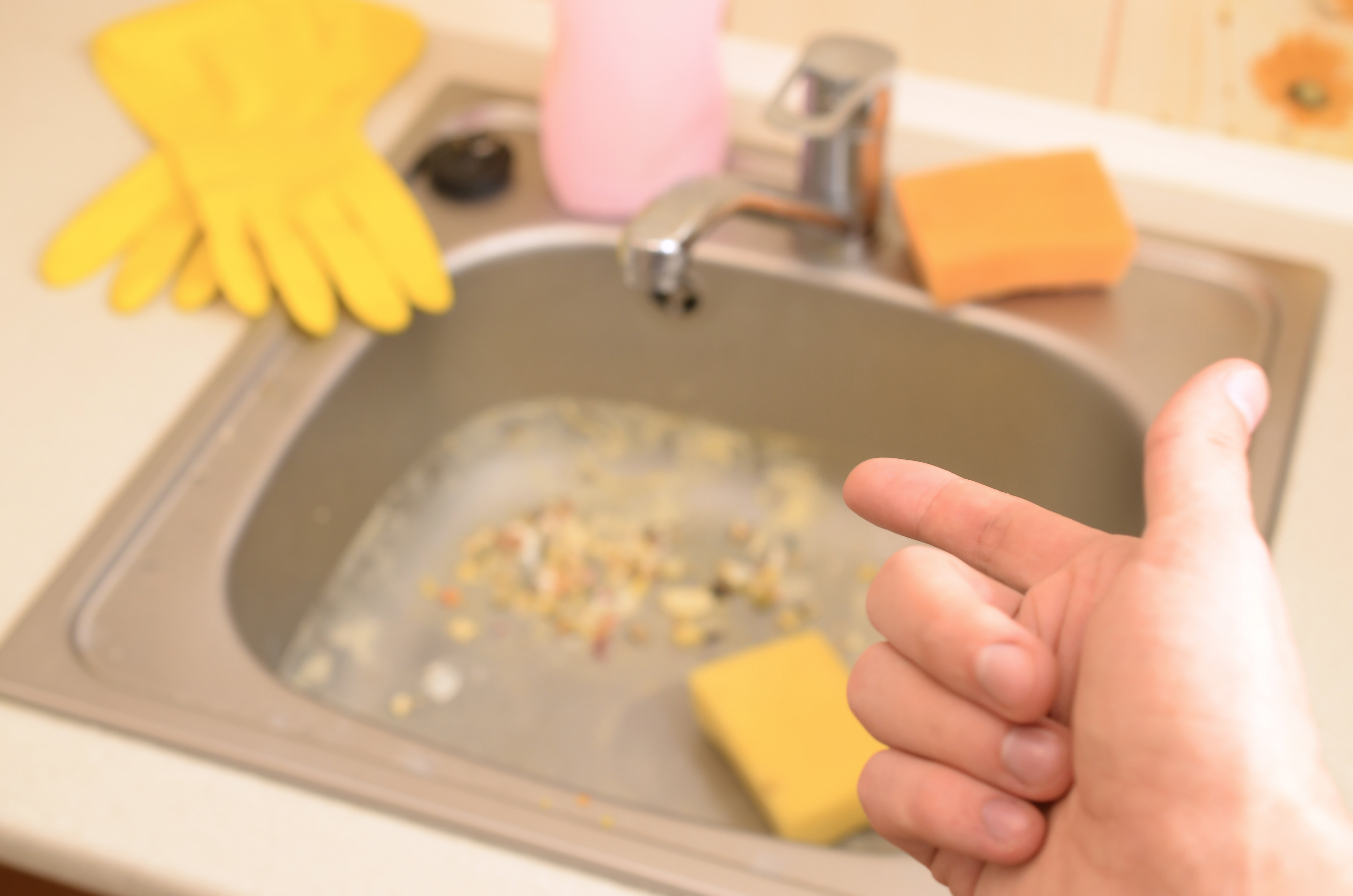 A mão aponta para a pia da cozinha suja com muitas partículas de alimentos antes da limpeza