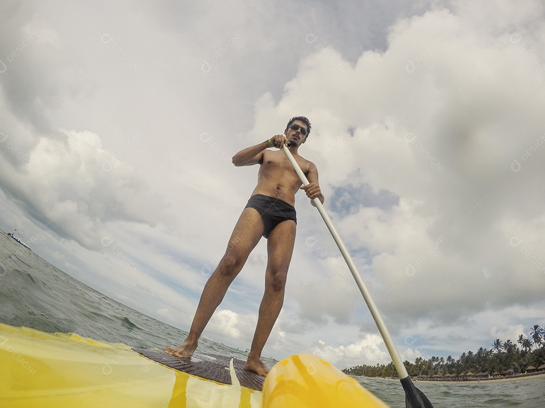Homem jovem negro se divertindo praticando Stand Up paddle no mar