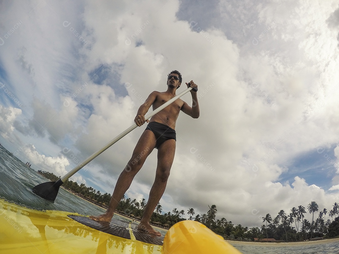 Homem jovem negro se divertindo praticando Stand Up paddle no mar