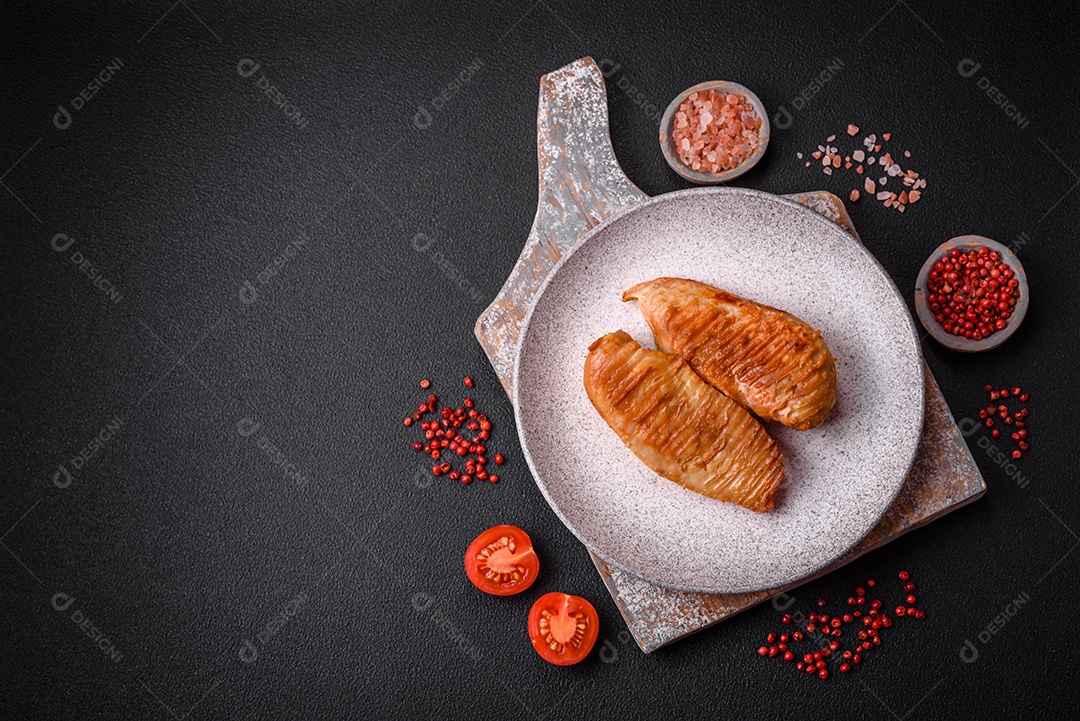 Delicioso filé de frango grelhado fresco com especiarias e ervas em um fundo escuro de concreto. Um prato cozido no fogo