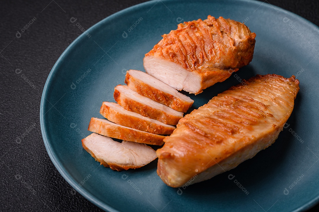 Delicioso filé de frango grelhado fresco com especiarias e ervas em um fundo escuro de concreto. Um prato cozido no fogo