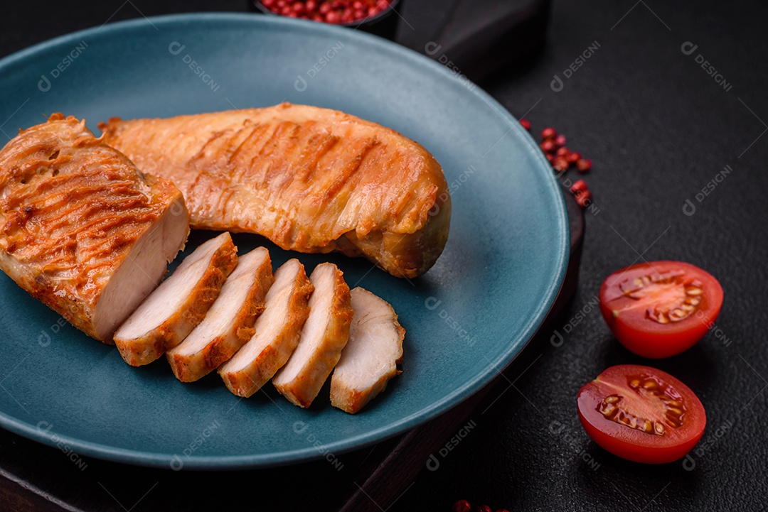 Delicioso filé de frango grelhado fresco com especiarias e ervas em um fundo escuro de concreto. Um prato cozido no fogo