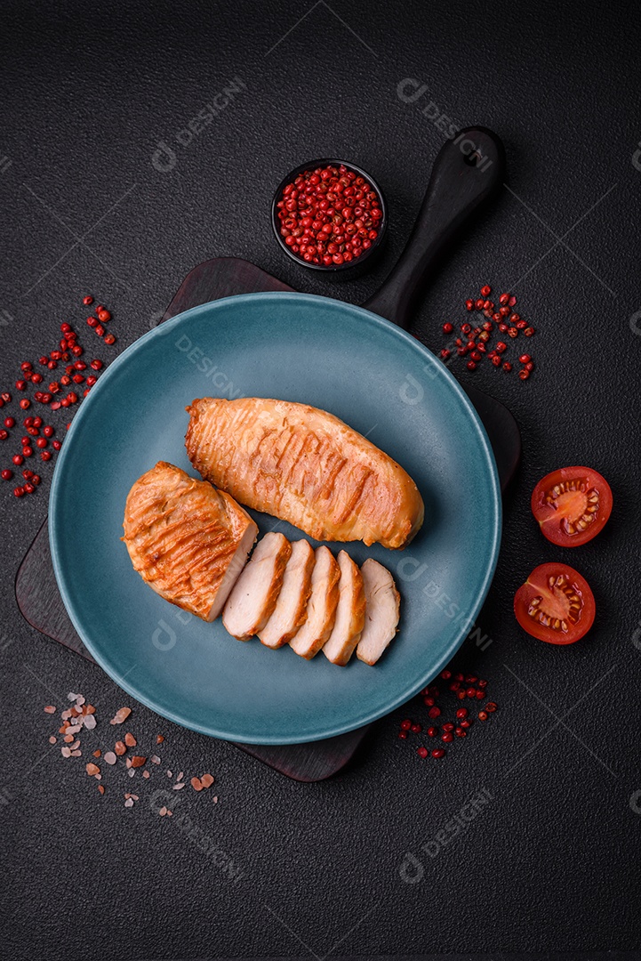 Delicioso filé de frango grelhado fresco com especiarias e ervas em um fundo escuro de concreto. Um prato cozido no fogo