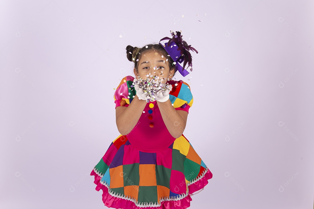 Linda menina fantasiada assoprando confetes sobre um fundo isolado branco.
