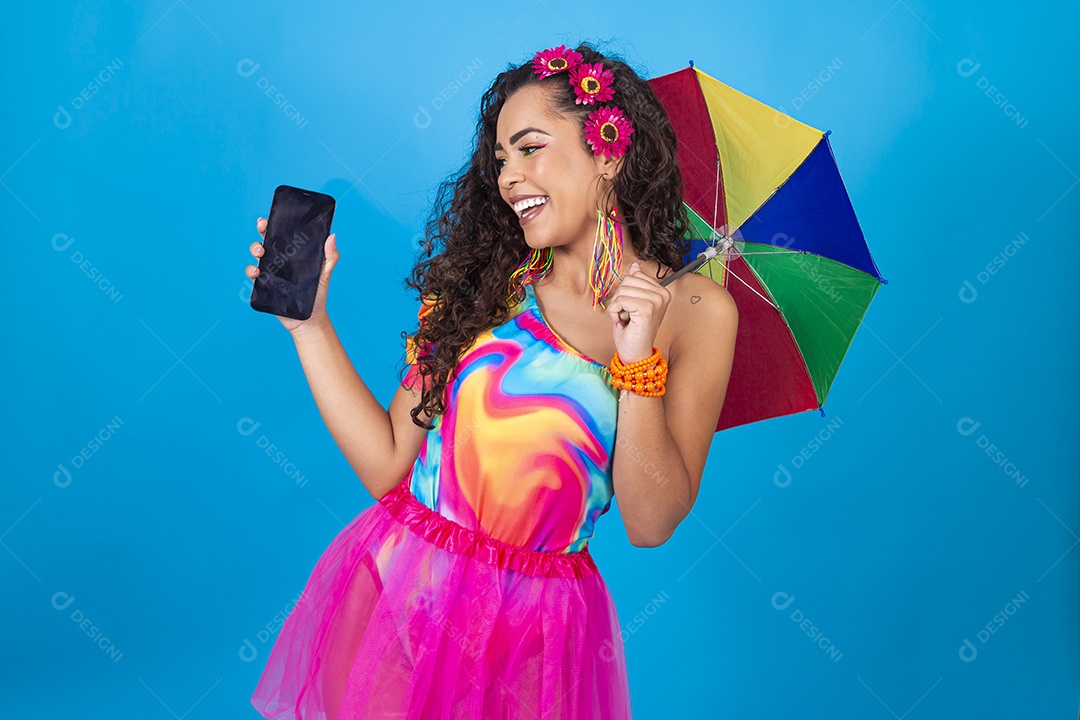 Mulher de cabelo cacheado com fantasia de carnaval estilo frevo segurando celular.