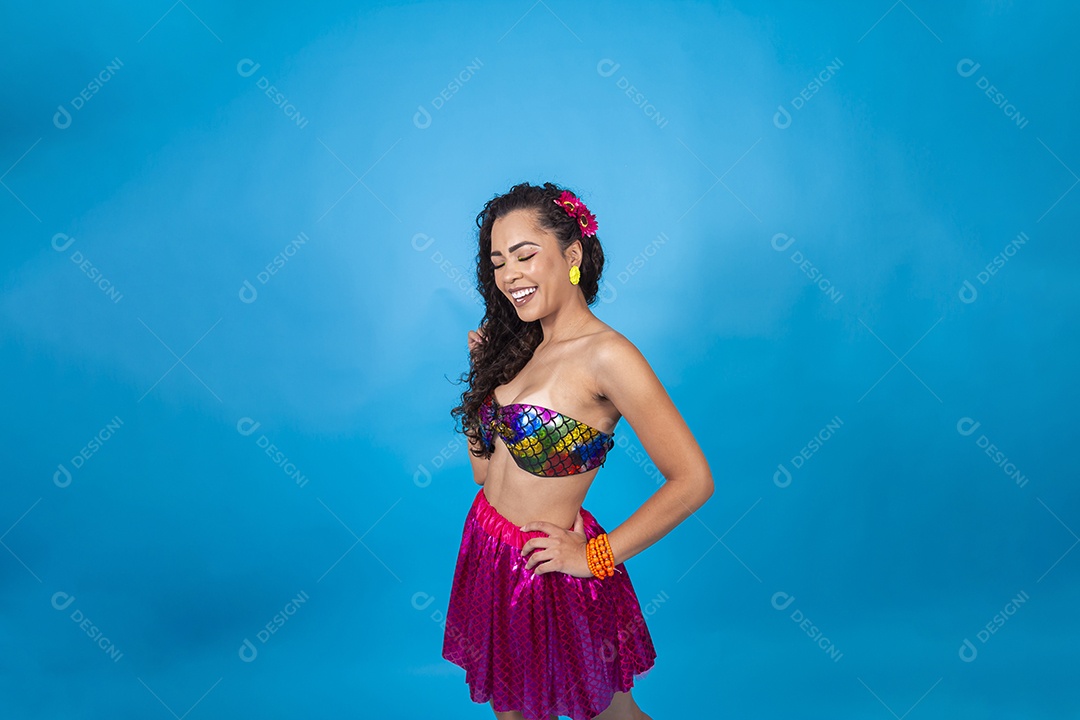 Linda mulher cabelo cacheado vestida com fantasia de carnaval sobre um fundo isolado azul.