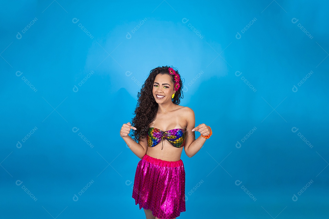 Linda mulher cabelo cacheado vestida com fantasia de carnaval sobre um fundo isolado azul.