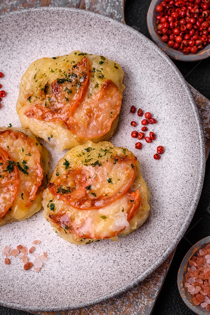 Delicioso filé de peixe assado com queijo, tomate, sal, especiarias e ervas sobre um fundo escuro de concreto