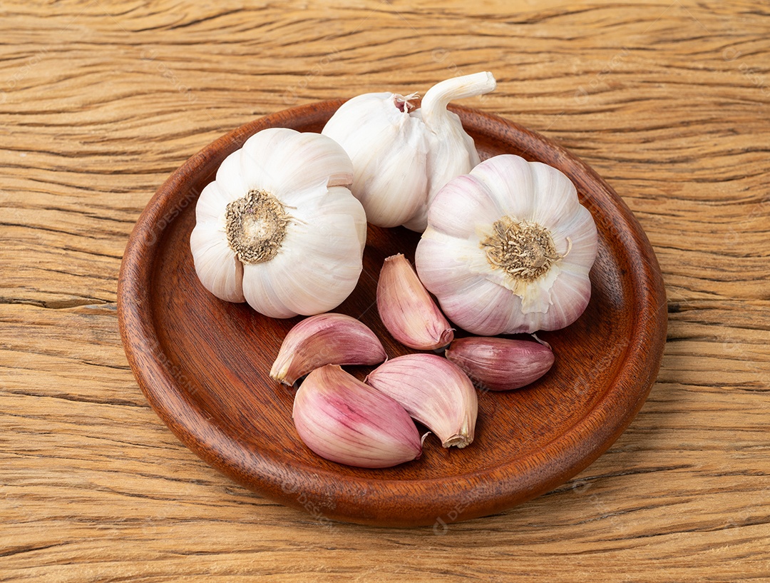 Cabeça de alho encima de tábua de madeira com dentes de alho ao lado