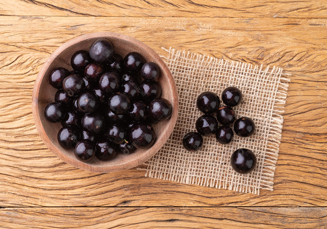 Tigela redonda com frutos da jabuticaba dentro sobre fundo de madeira