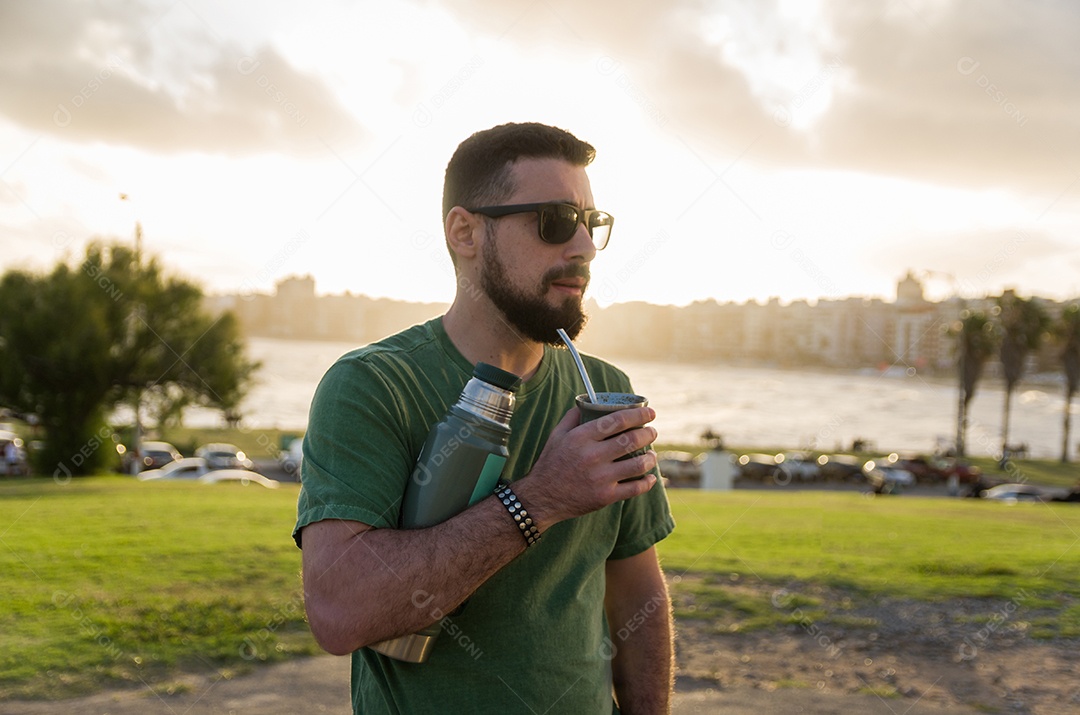 Homem bebendo chimarrão mate infusão de erva-mate com água quente ao pôr do sol no Uruguai