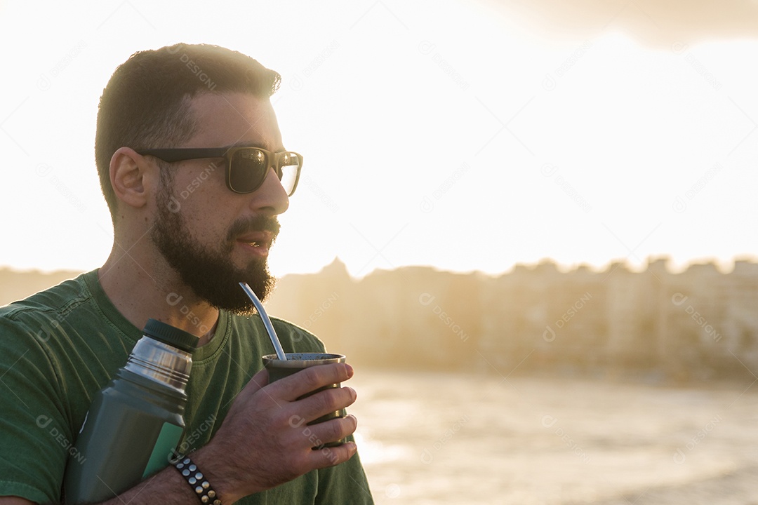 Homem bebendo chimarrão mate infusão de erva-mate com água quente ao pôr do sol no Uruguai