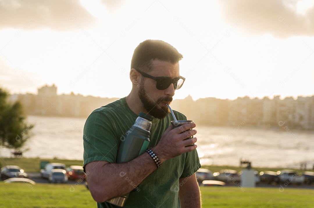 Homem bebendo chimarrão mate infusão de erva-mate com água quente ao pôr do sol no Uruguai