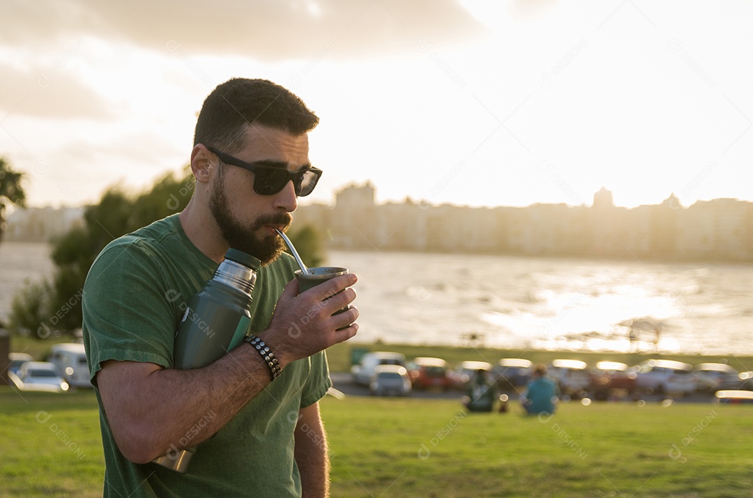 Homem bebendo chimarrão mate infusão de erva-mate com água quente ao pôr do sol no Uruguai