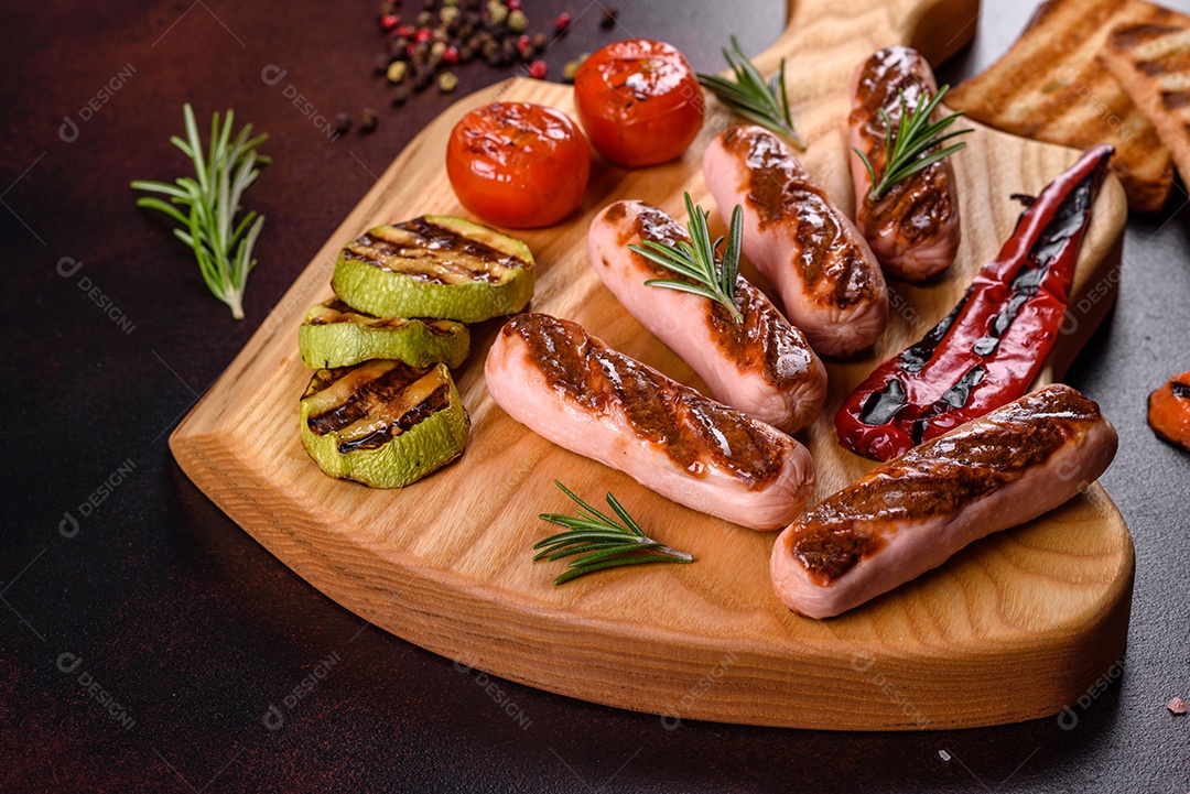Saborosos enchidos frescos grelhados com legumes, especiarias e ervas. Foto do prato acabado em uma mesa de concreto escuro