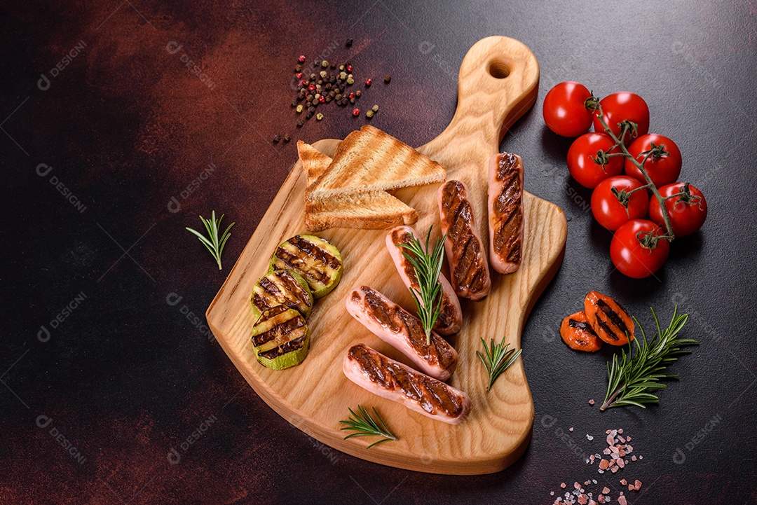 Saborosos enchidos frescos grelhados com legumes, especiarias e ervas. Foto do prato acabado em uma mesa de concreto escuro