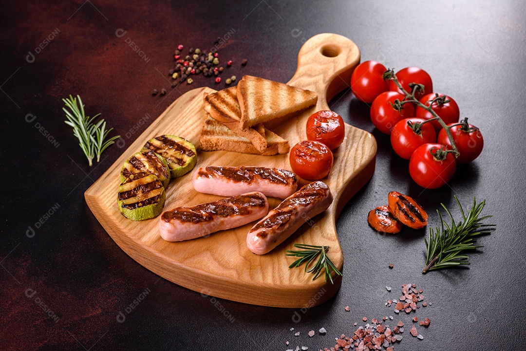 Saborosos enchidos frescos grelhados com legumes, especiarias e ervas. Foto do prato acabado em uma mesa de concreto escuro