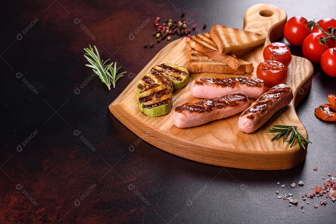 Saborosos enchidos frescos grelhados com legumes, especiarias e ervas. Foto do prato acabado em uma mesa de concreto escuro