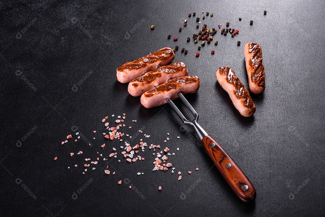 Saborosos enchidos frescos grelhados com legumes, especiarias e ervas. Foto do prato acabado em uma mesa de concreto escuro