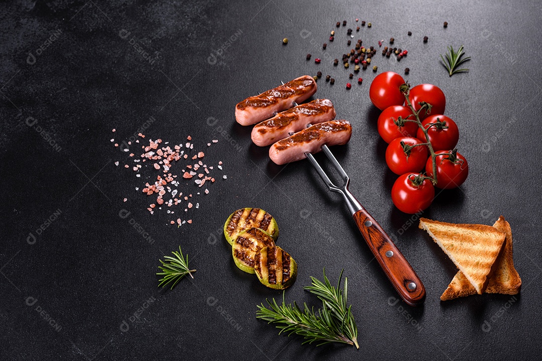 Saborosos enchidos frescos grelhados com legumes, especiarias e ervas. Foto do prato acabado em uma mesa de concreto escuro