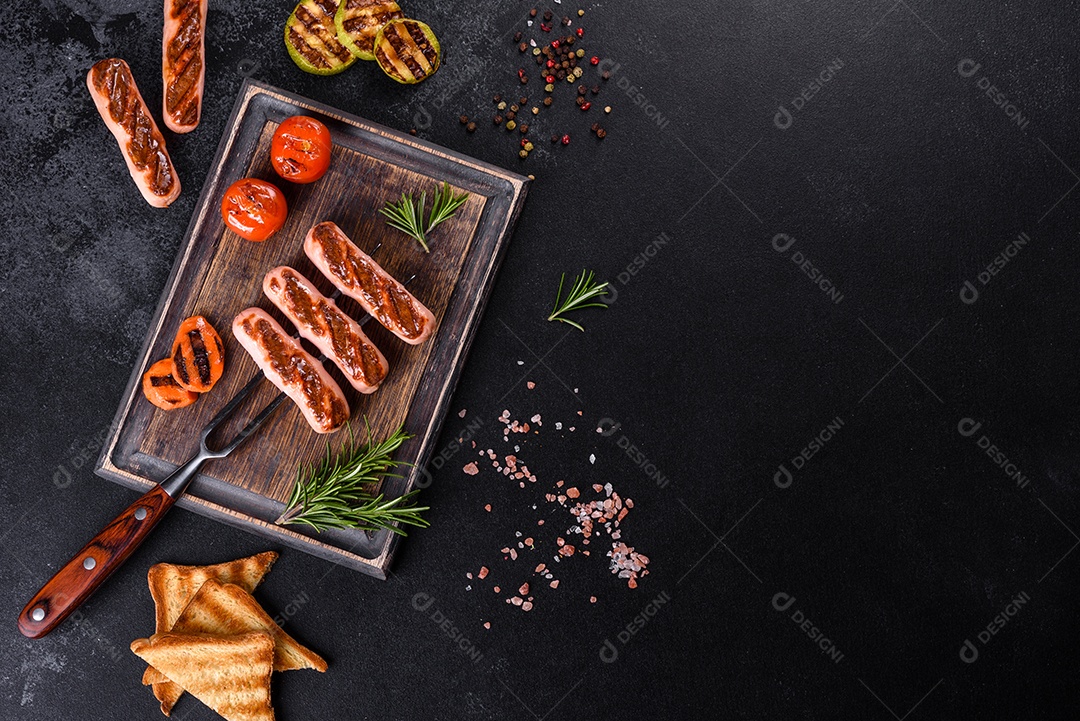 Saborosos enchidos frescos grelhados com legumes, especiarias e ervas. Foto do prato acabado em uma mesa de concreto escuro