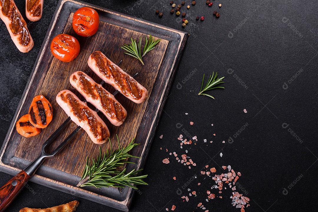Saborosos enchidos frescos grelhados com legumes, especiarias e ervas. Foto do prato acabado em uma mesa de concreto escuro