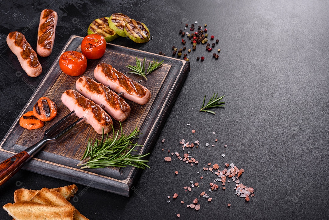 Saborosos enchidos frescos grelhados com legumes, especiarias e ervas. Foto do prato acabado em uma mesa de concreto escuro