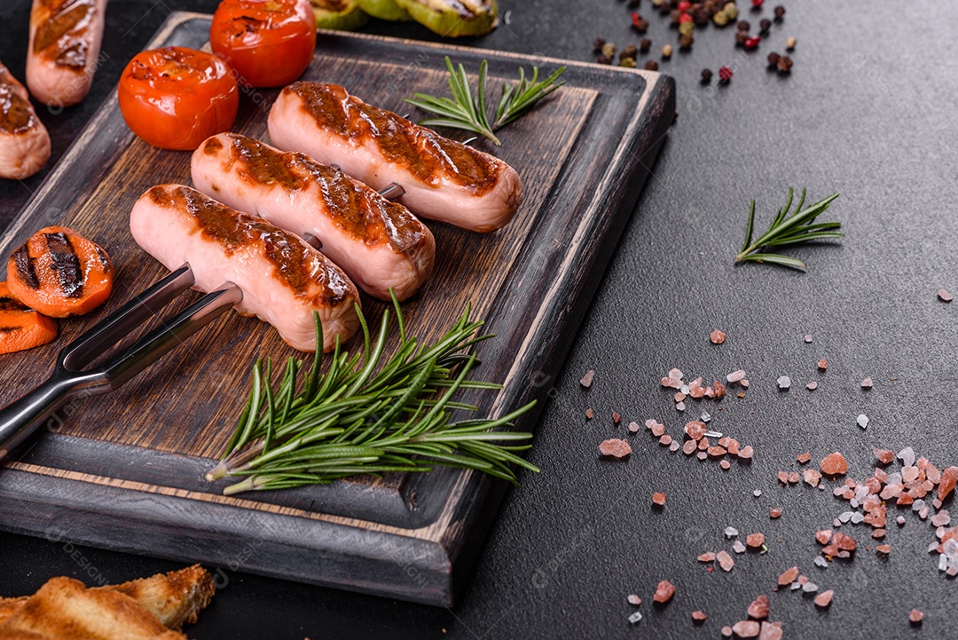 Saborosos enchidos frescos grelhados com legumes, especiarias e ervas. Foto do prato acabado em uma mesa de concreto escuro