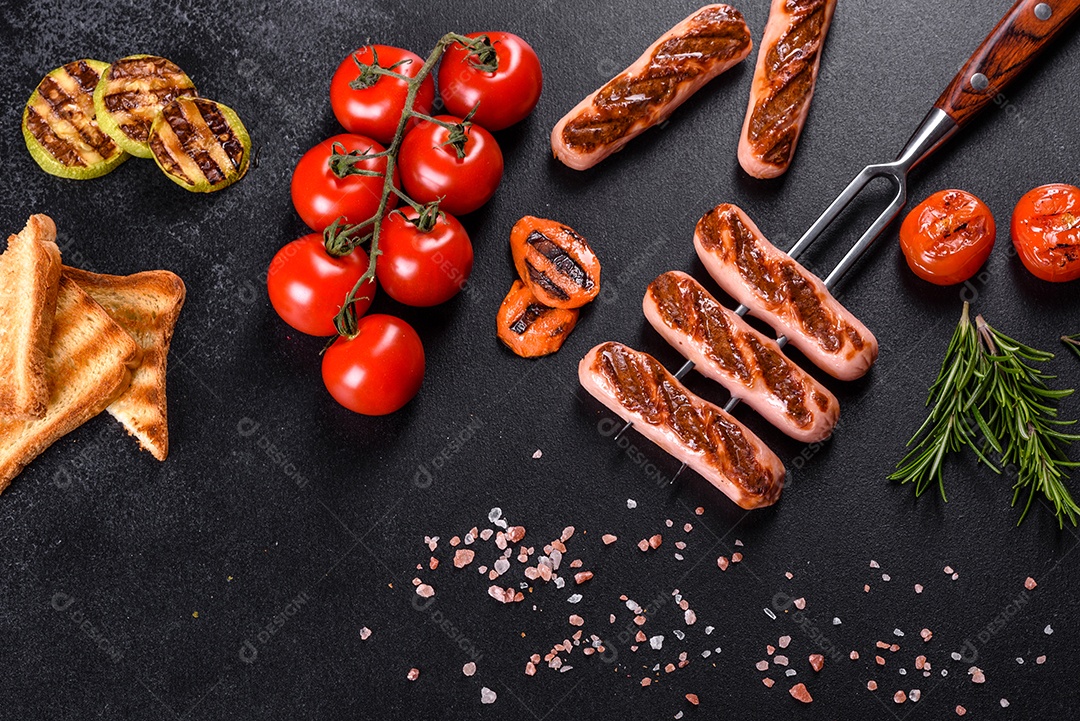 Saborosos enchidos frescos grelhados com legumes, especiarias e ervas. Foto do prato acabado em uma mesa de concreto escuro