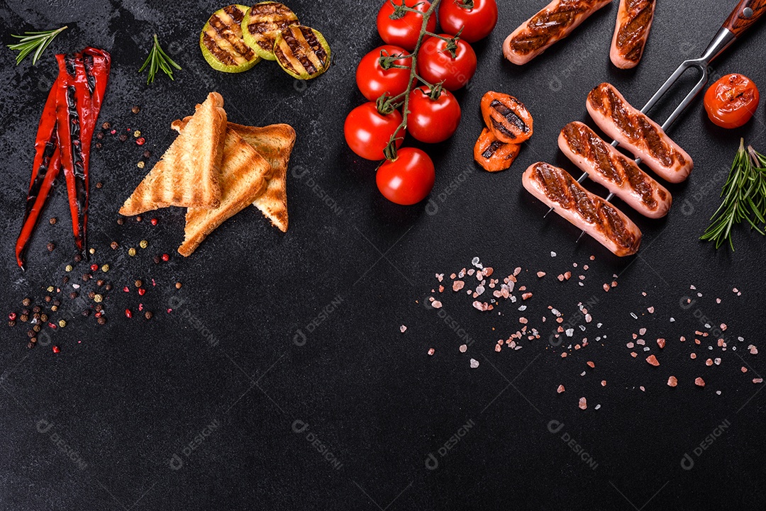 Saborosos enchidos frescos grelhados com legumes, especiarias e ervas. Foto do prato acabado em uma mesa de concreto escuro