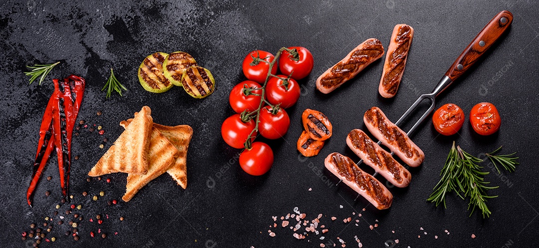 Saborosos enchidos frescos grelhados com legumes, especiarias e ervas. Foto do prato acabado em uma mesa de concreto escuro