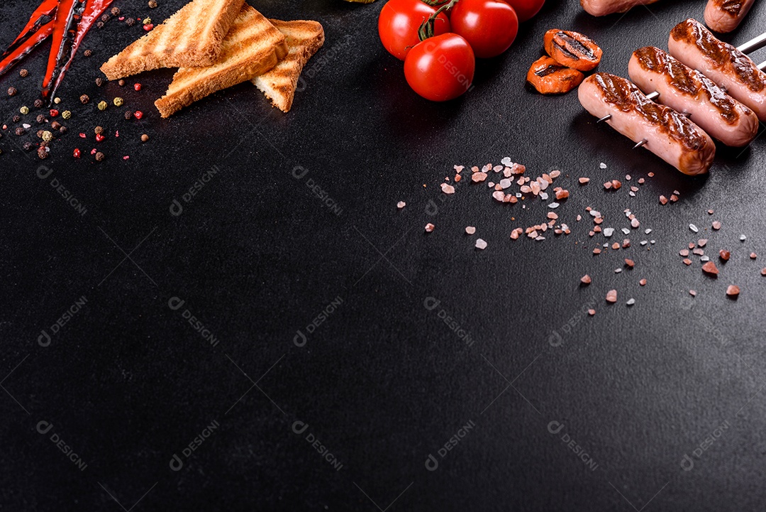 Saborosos enchidos frescos grelhados com legumes, especiarias e ervas. Foto do prato acabado em uma mesa de concreto escuro