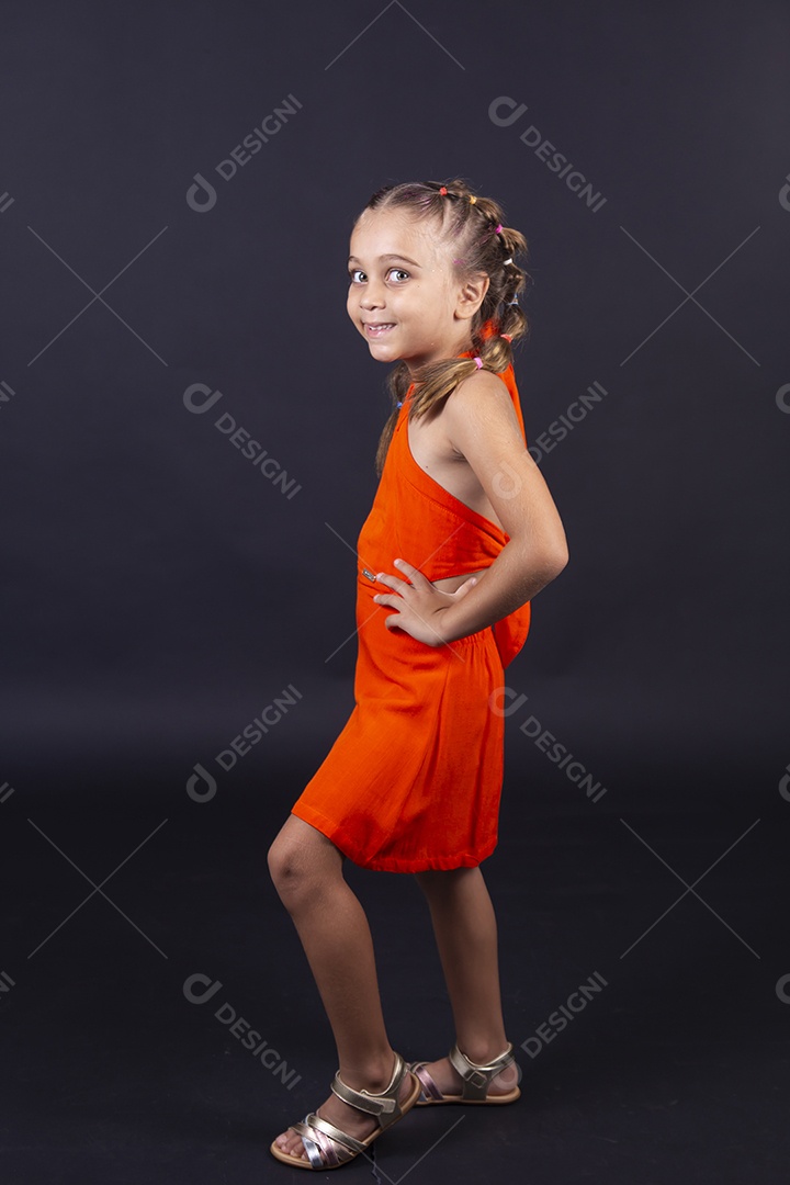 Linda menina usando vestido laranja sobre um fundo isolado preto.