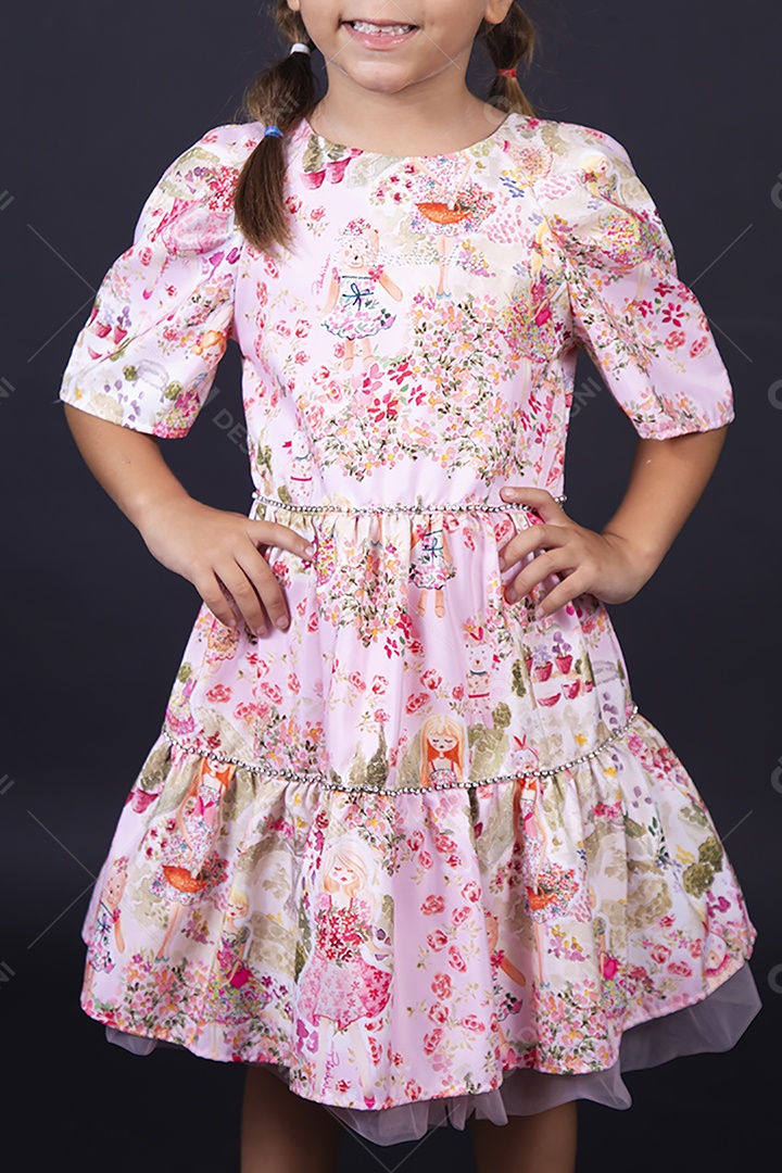 Criança usando vestido florido sobre um fundo isolado preto.