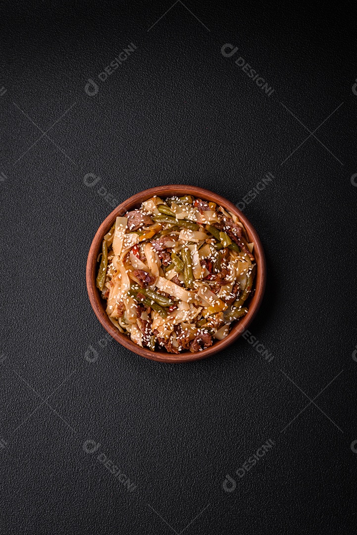 Delicioso prato asiático udon com pimenta, feijão verde, especiarias e ervas em uma placa cerâmica sobre um fundo escuro de concreto