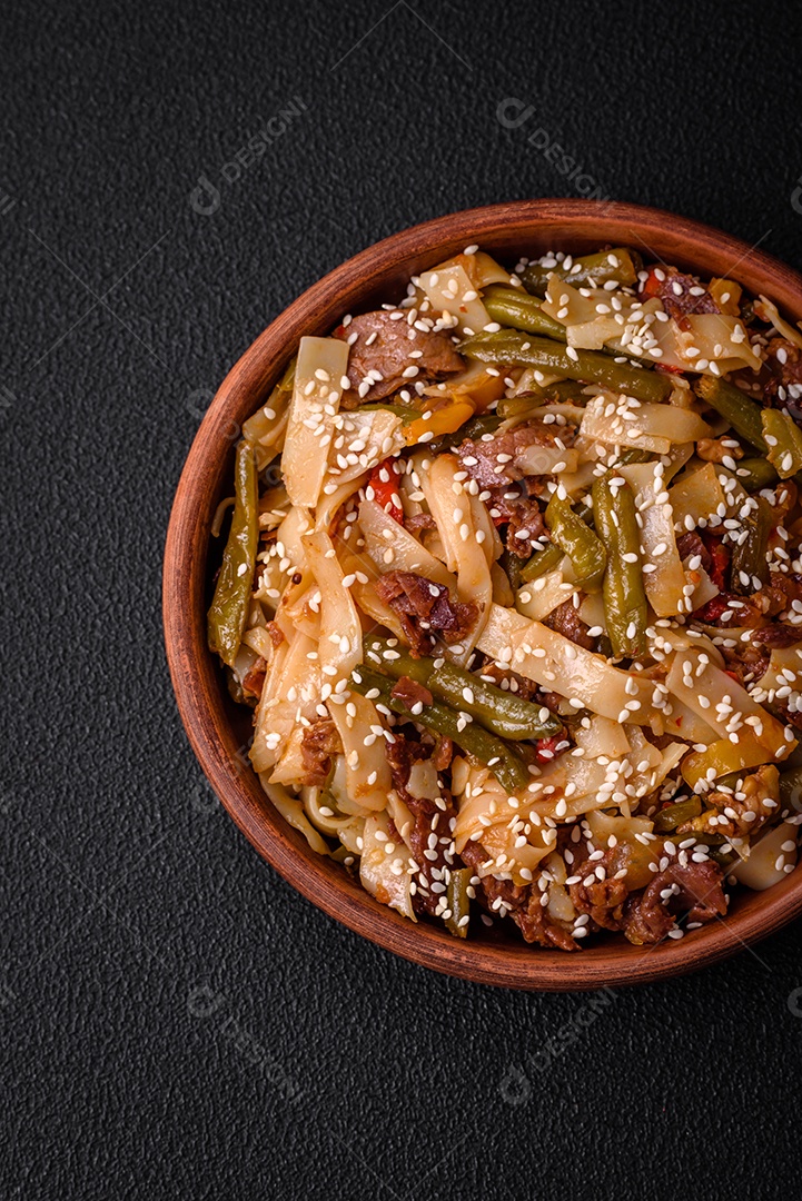 Delicioso prato asiático udon com pimenta, feijão verde, especiarias e ervas em uma placa cerâmica sobre um fundo escuro de concreto