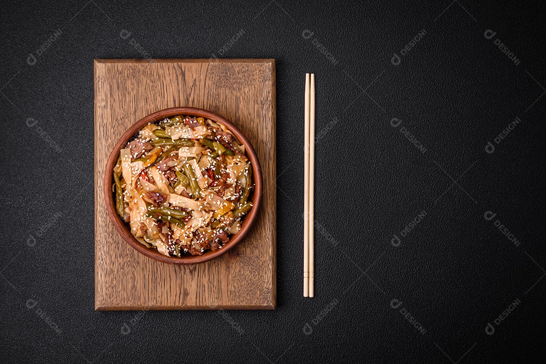Delicioso prato asiático udon com pimenta, feijão verde, especiarias e ervas em uma placa cerâmica sobre um fundo escuro de concreto