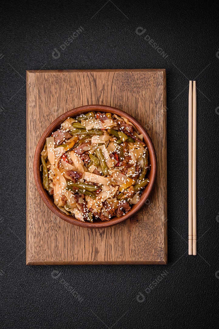 Delicioso prato asiático udon com pimenta, feijão verde, especiarias e ervas em uma placa cerâmica sobre um fundo escuro de concreto