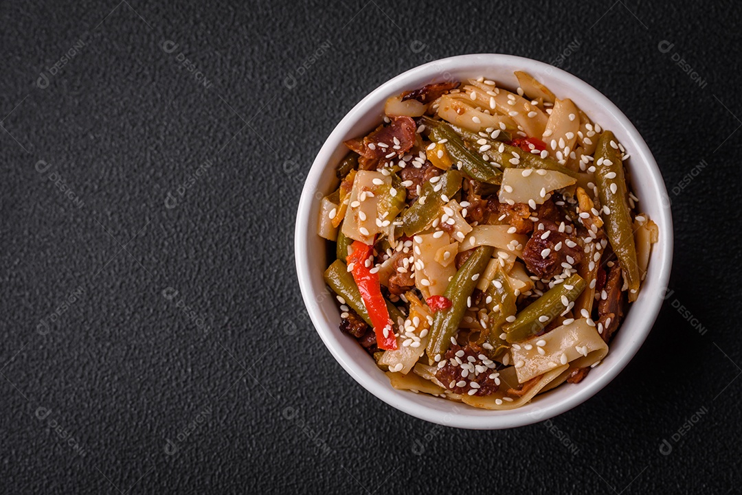 Delicioso prato asiático udon com pimenta, feijão verde, especiarias e ervas em uma placa cerâmica sobre um fundo escuro de concreto