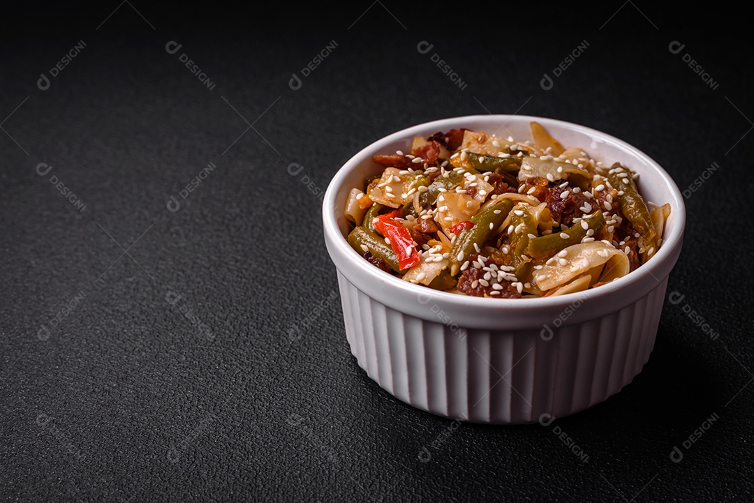 Delicioso prato asiático udon com pimenta, feijão verde, especiarias e ervas em uma placa cerâmica sobre um fundo escuro de concreto