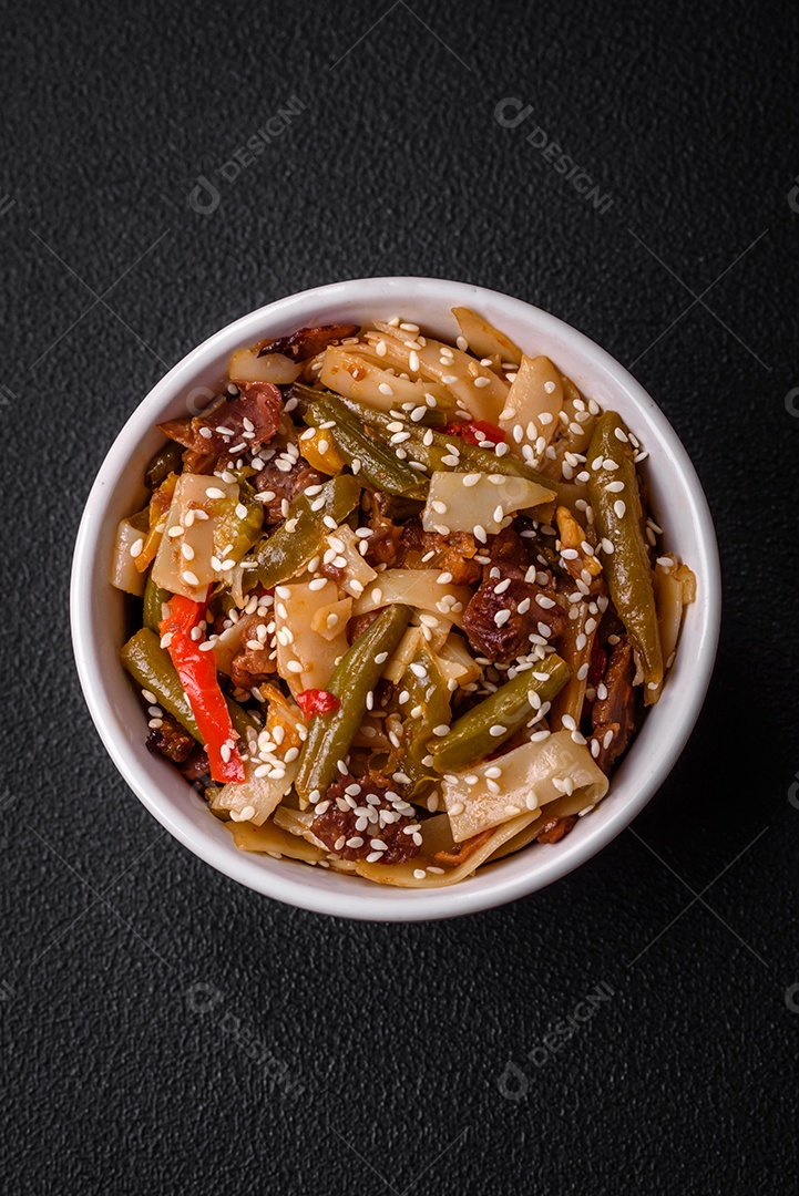 Delicioso prato asiático udon com pimenta, feijão verde, especiarias e ervas em uma placa cerâmica sobre um fundo escuro de concreto