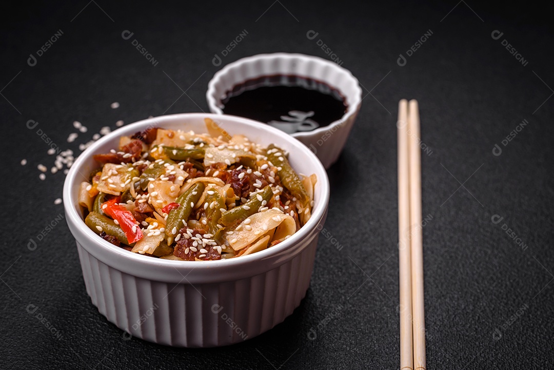 Delicioso prato asiático udon com pimenta, feijão verde, especiarias e ervas em uma placa cerâmica sobre um fundo escuro de concreto