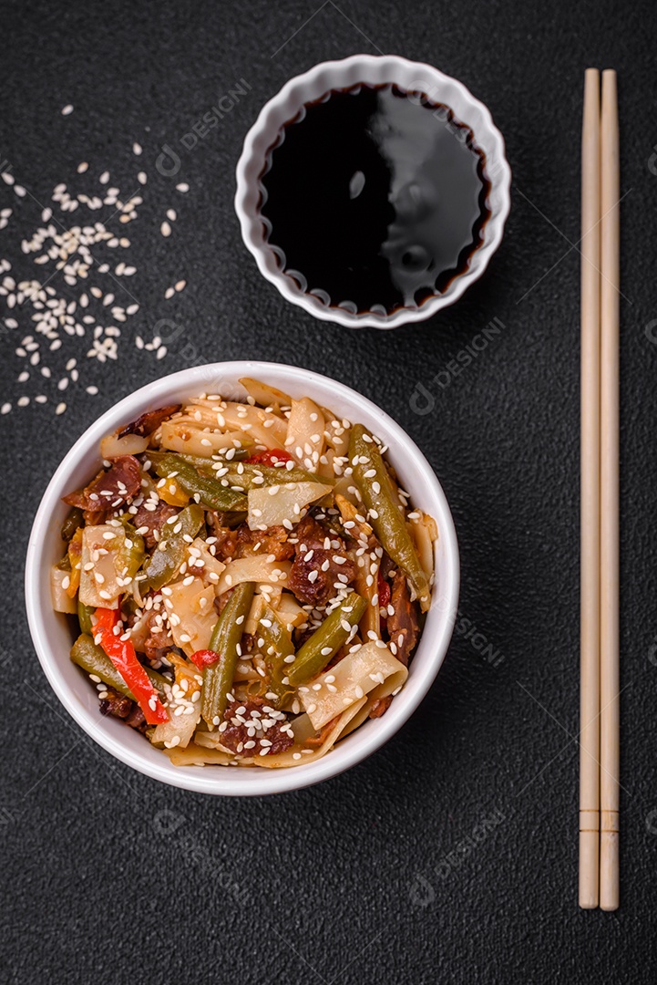 Delicioso prato asiático udon com pimenta, feijão verde, especiarias e ervas em uma placa cerâmica sobre um fundo escuro de concreto
