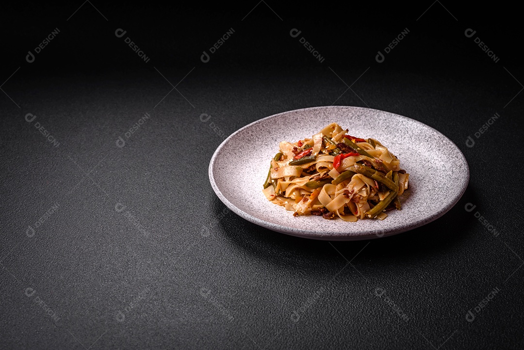 Delicioso prato asiático udon com pimenta, feijão verde, especiarias e ervas em uma placa cerâmica sobre um fundo escuro de concreto