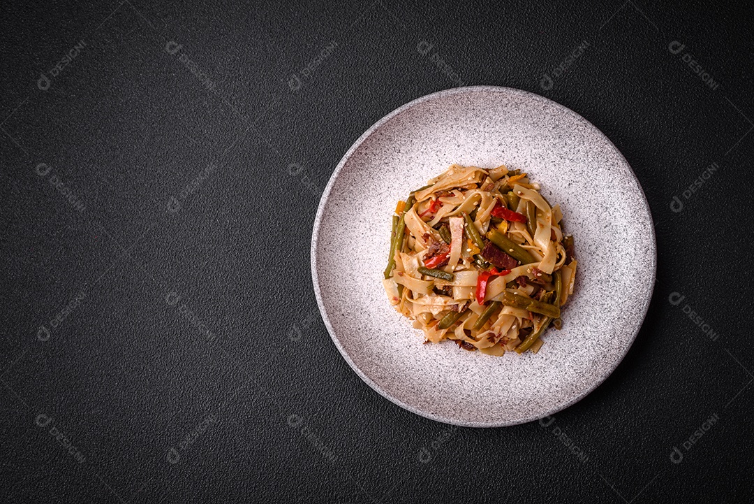 Delicioso prato asiático udon com pimenta, feijão verde, especiarias e ervas em uma placa cerâmica sobre um fundo escuro de concreto