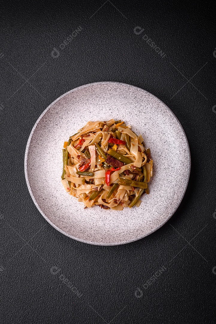 Delicioso prato asiático udon com pimenta, feijão verde, especiarias e ervas em uma placa cerâmica sobre um fundo escuro de concreto