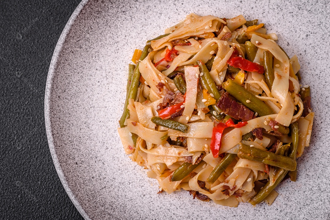 Delicioso prato asiático udon com pimenta, feijão verde, especiarias e ervas em uma placa cerâmica sobre um fundo escuro de concreto