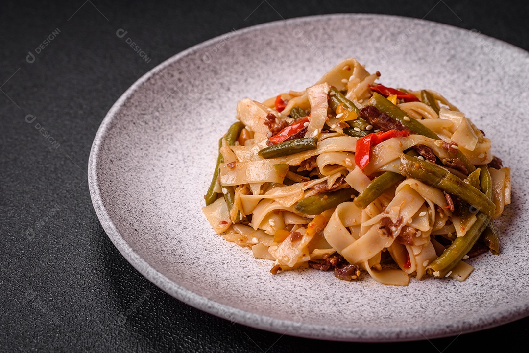 Delicioso prato asiático udon com pimenta, feijão verde, especiarias e ervas em uma placa cerâmica sobre um fundo escuro de concreto