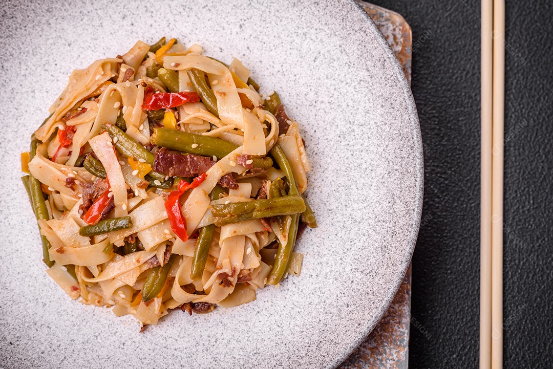 Delicioso prato asiático udon com pimenta, feijão verde, especiarias e ervas em uma placa cerâmica sobre um fundo escuro de concreto