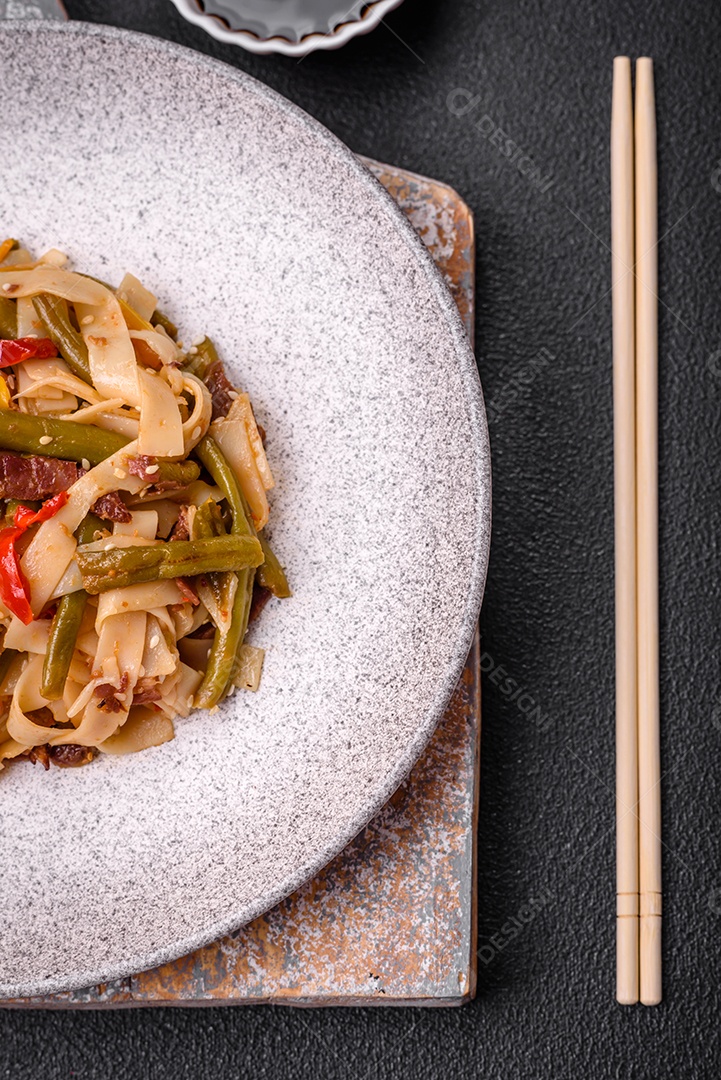 Delicioso prato asiático udon com pimenta, feijão verde, especiarias e ervas em uma placa cerâmica sobre um fundo escuro de concreto